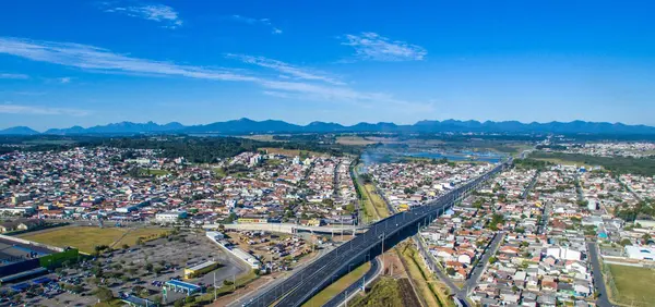 Vista aérea de Pinhais com a rodovia, os bairros ao redor do Jardim Amélia e o Parque das Águas ao fundo